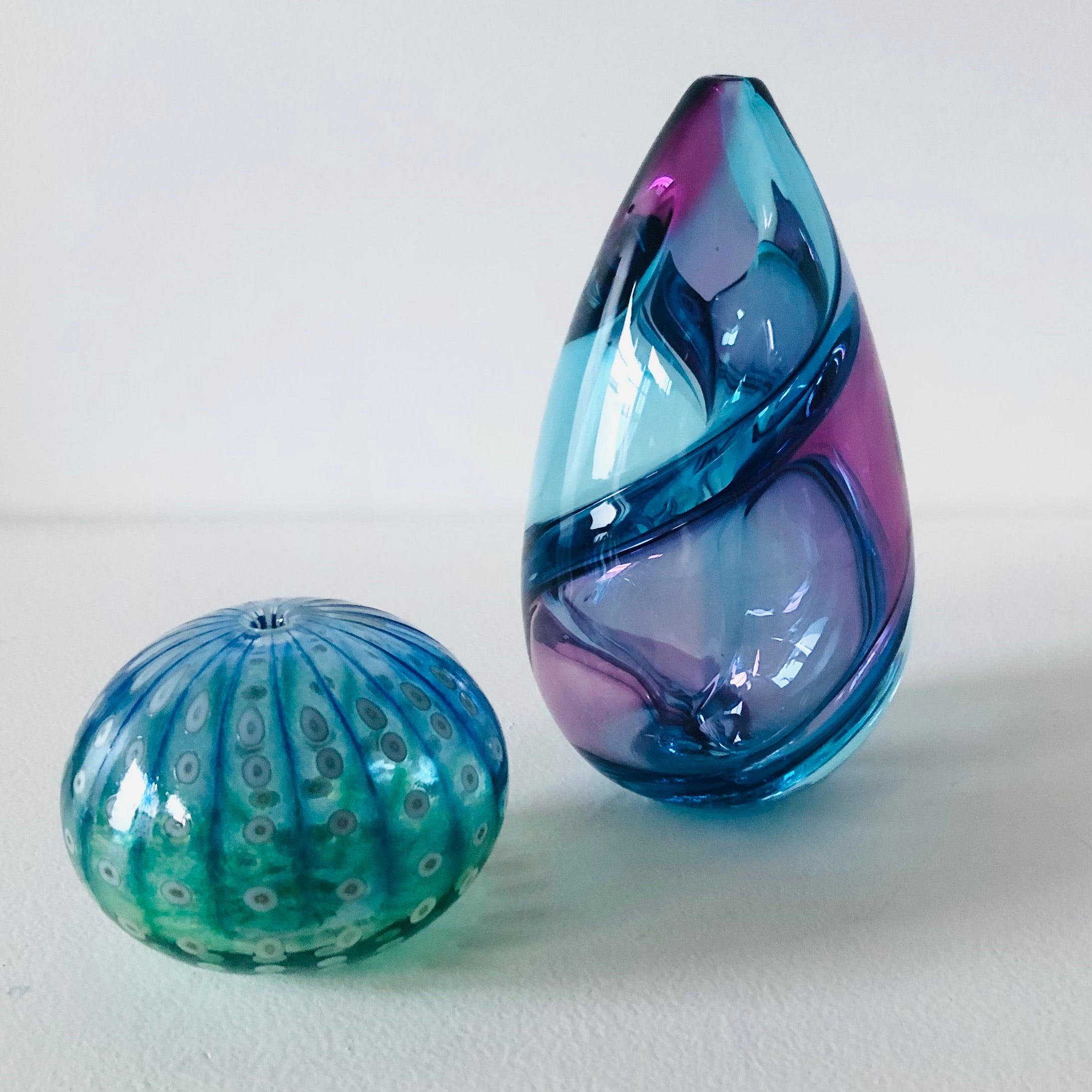 Two glass artworks, one shaped like a kina and the other egg-shaped