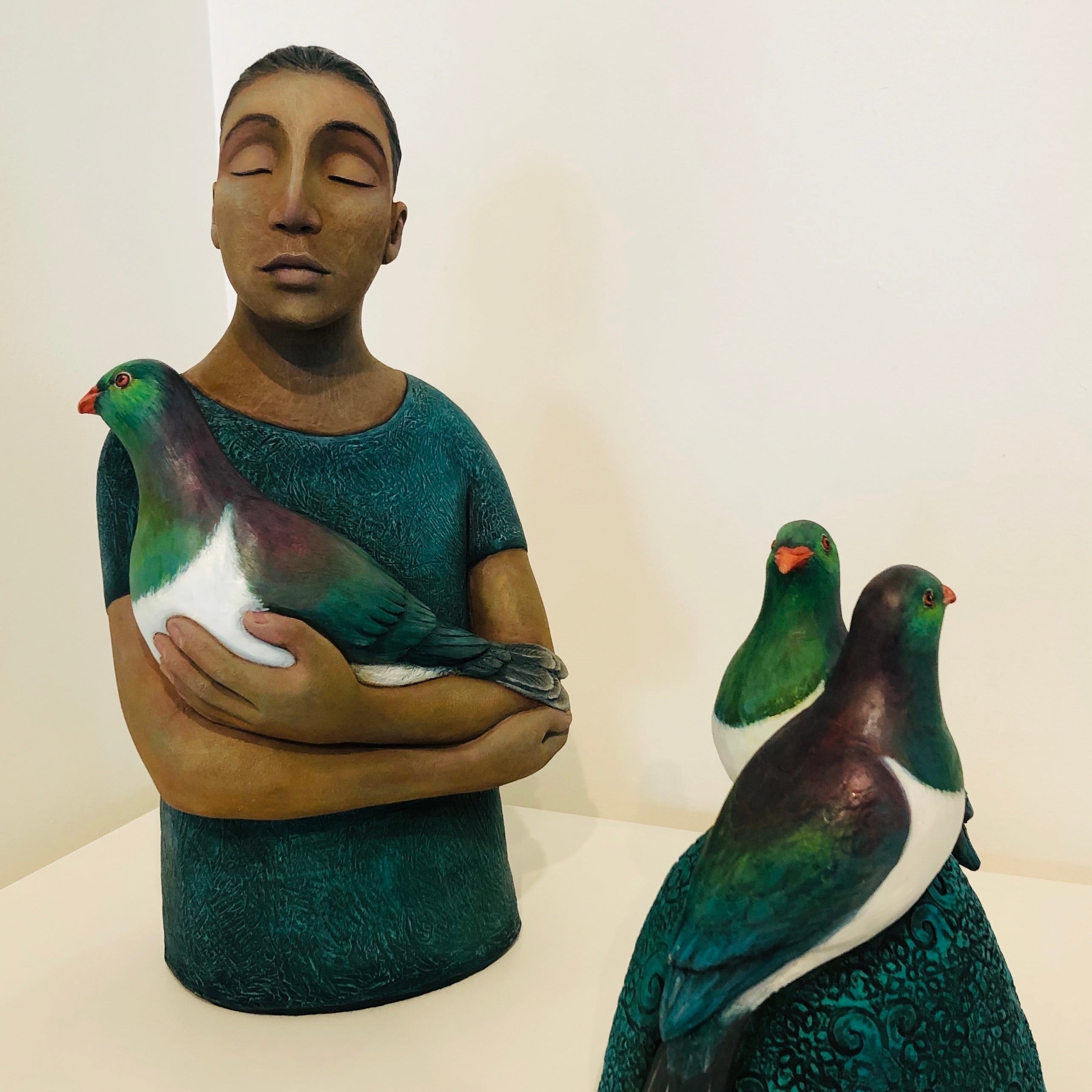 Sculpture of person holding a kereru/wood pigeon, next to a separate sculpture of kereru