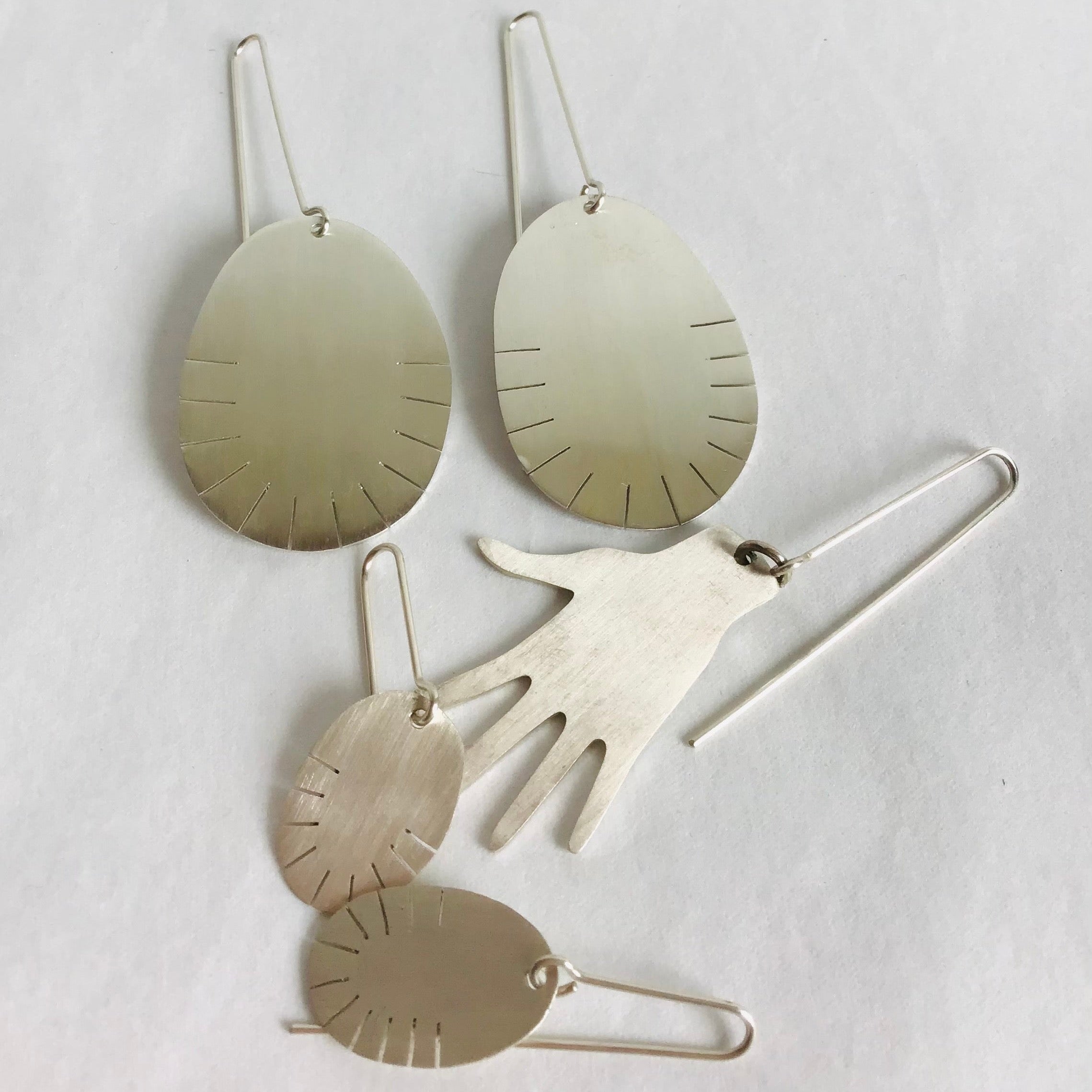 Collection of silver earrings, two oval pairs, and one pair hand-shaped